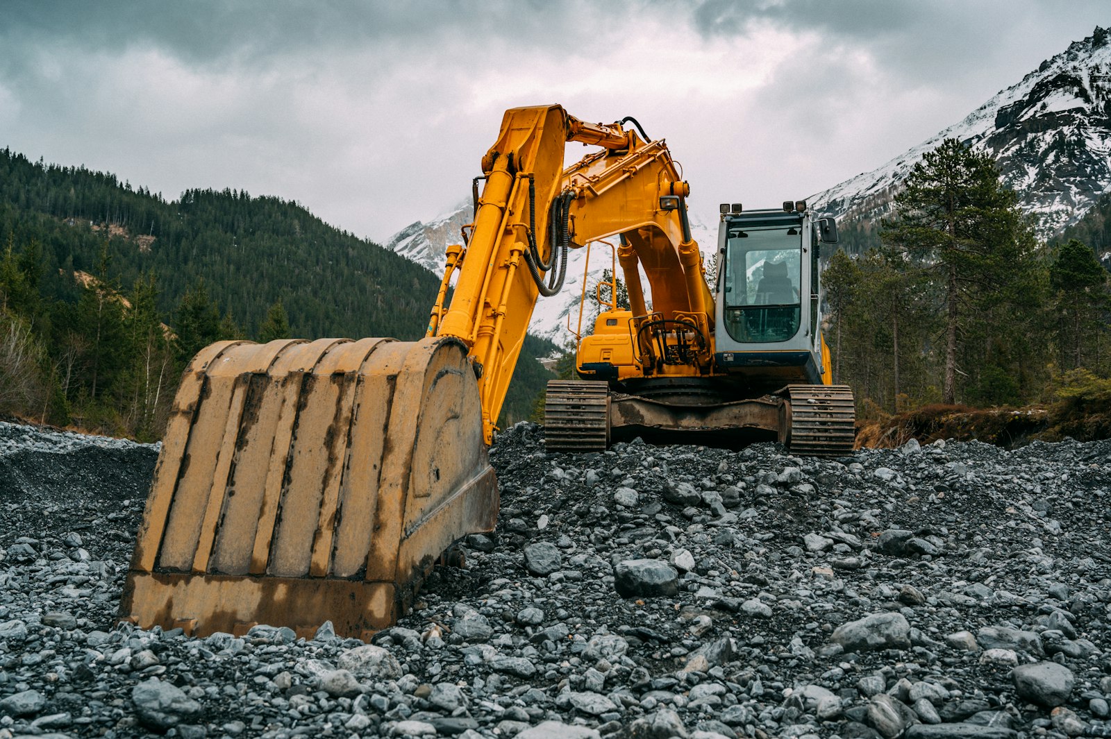 Yellow tracked excavator with its bucket set down on a stony riverbed